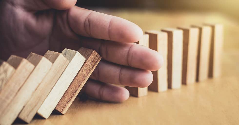 An image of a hand between falling dominoes.